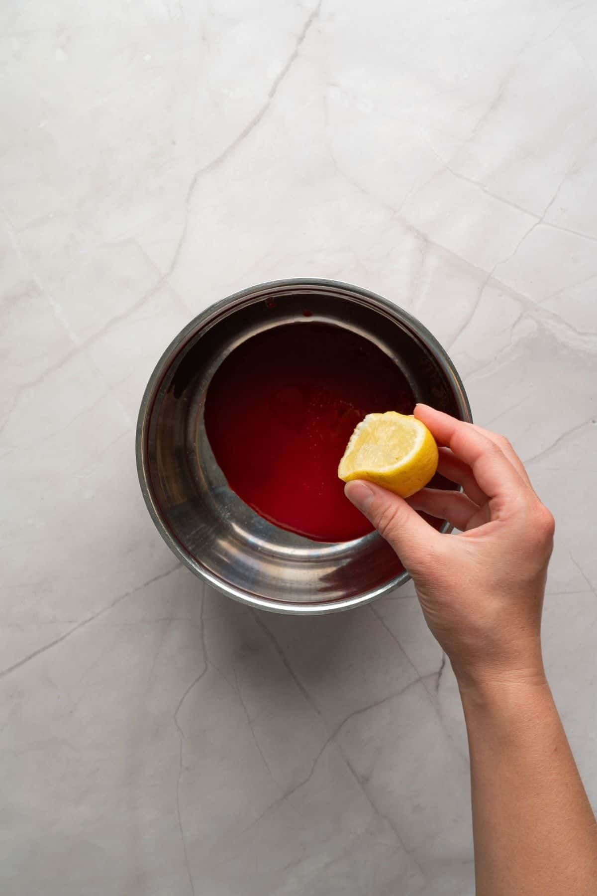 A hand squeezing lemon on a raspberry mixture in a bowl.
