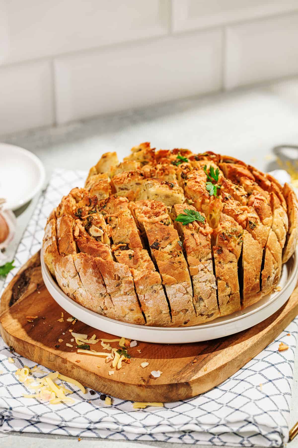 A golden, cheesy pull-apart garlic bread garnished with fresh parsley, served on a plate placed on a wooden board, with melted cheese oozing between the cuts.