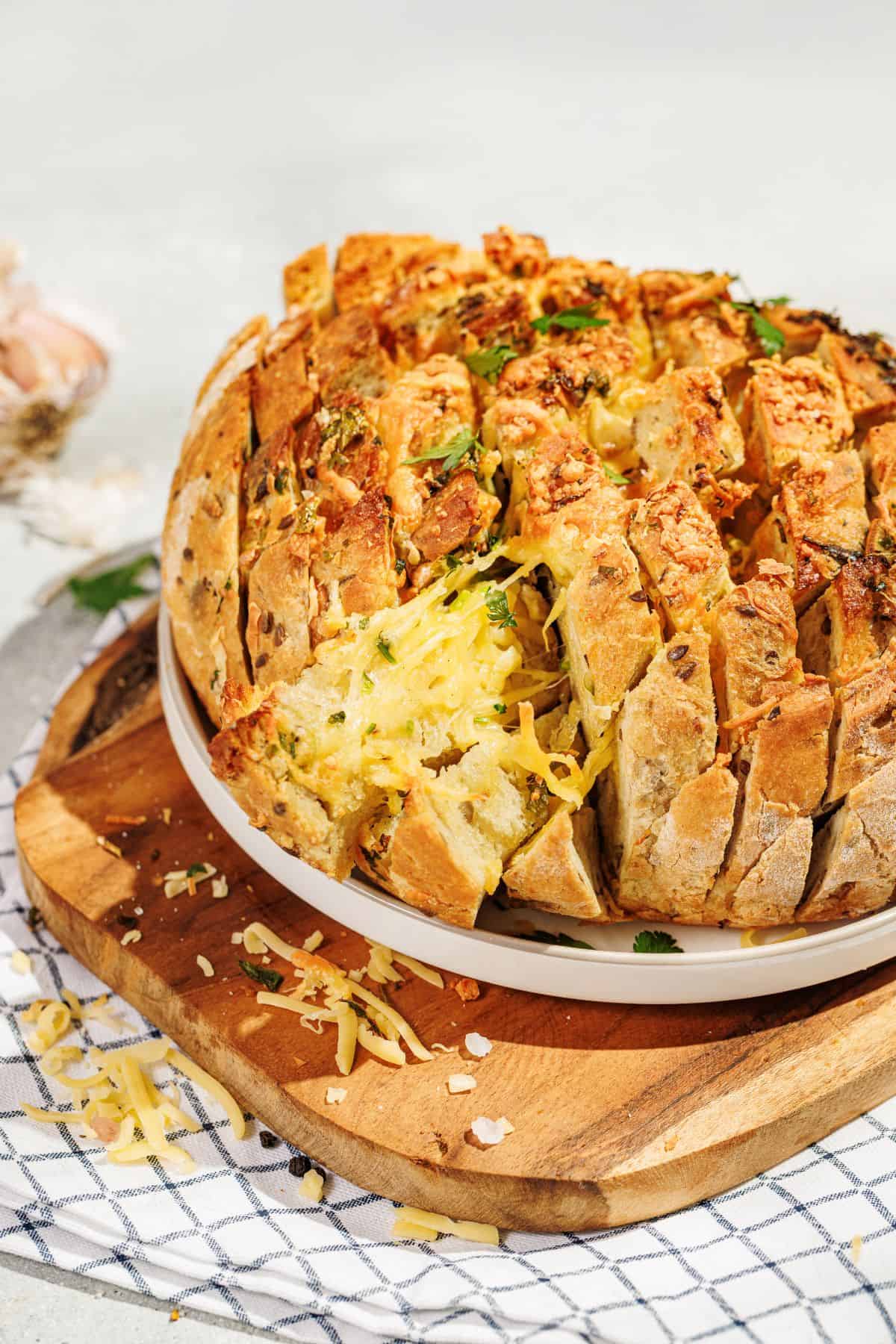 A golden, cheesy pull-apart garlic bread garnished with fresh parsley, served on a plate placed on a wooden board, with melted cheese oozing between the cuts.