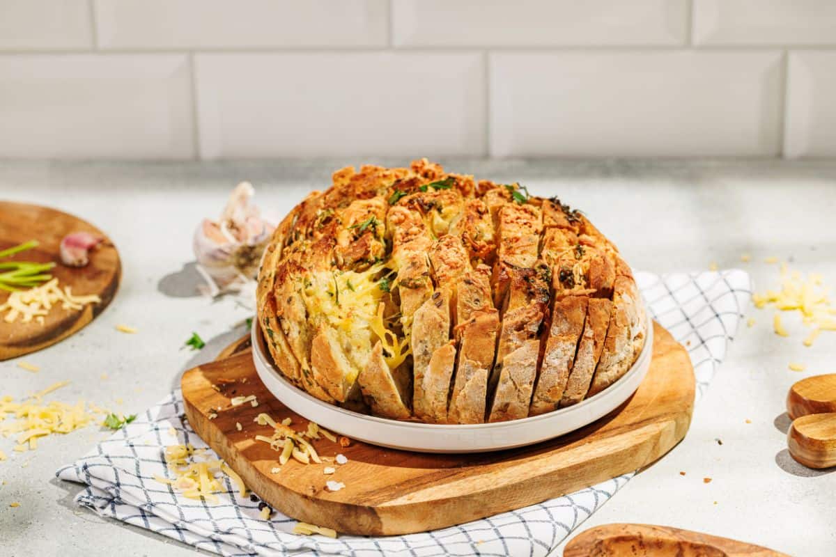 A golden, cheesy pull-apart garlic bread garnished with fresh parsley, served on a plate placed on a wooden board, with melted cheese oozing between the cuts.