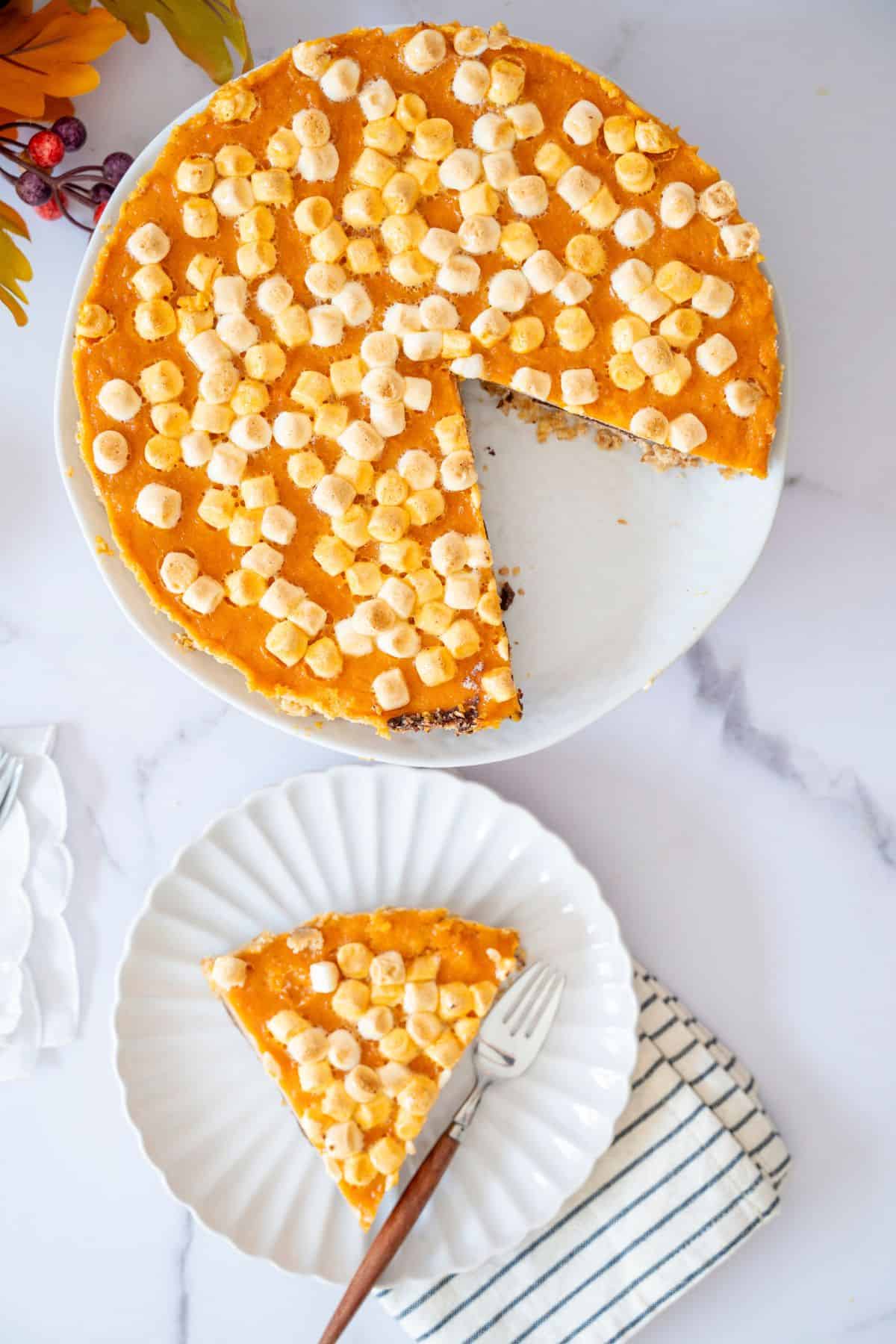 A sliced sweet potato pie in a serving dish with one slice placed on a plate beside it.