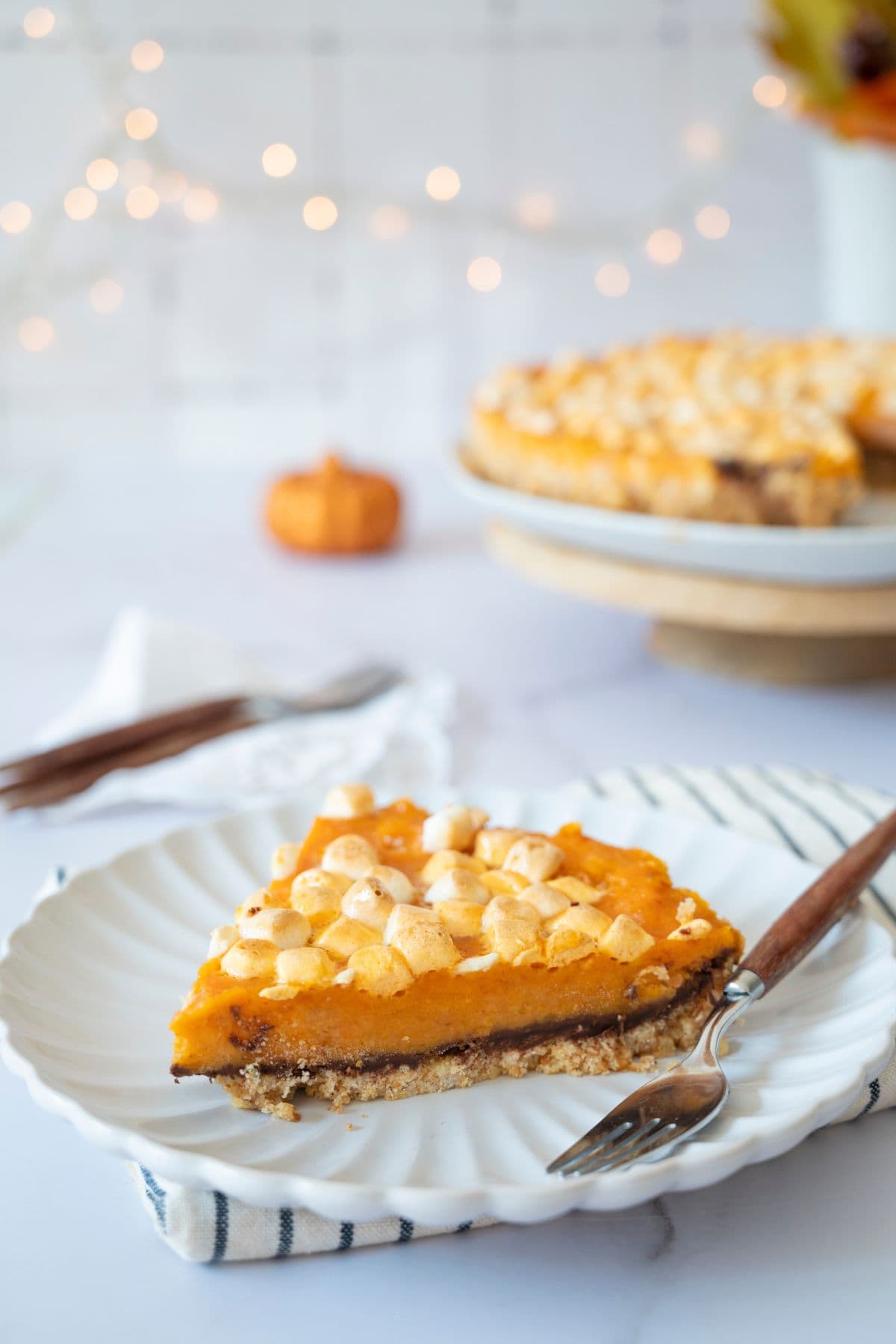 A slice of sweet potato pie served on a plate with the whole pie blurred in the background.
