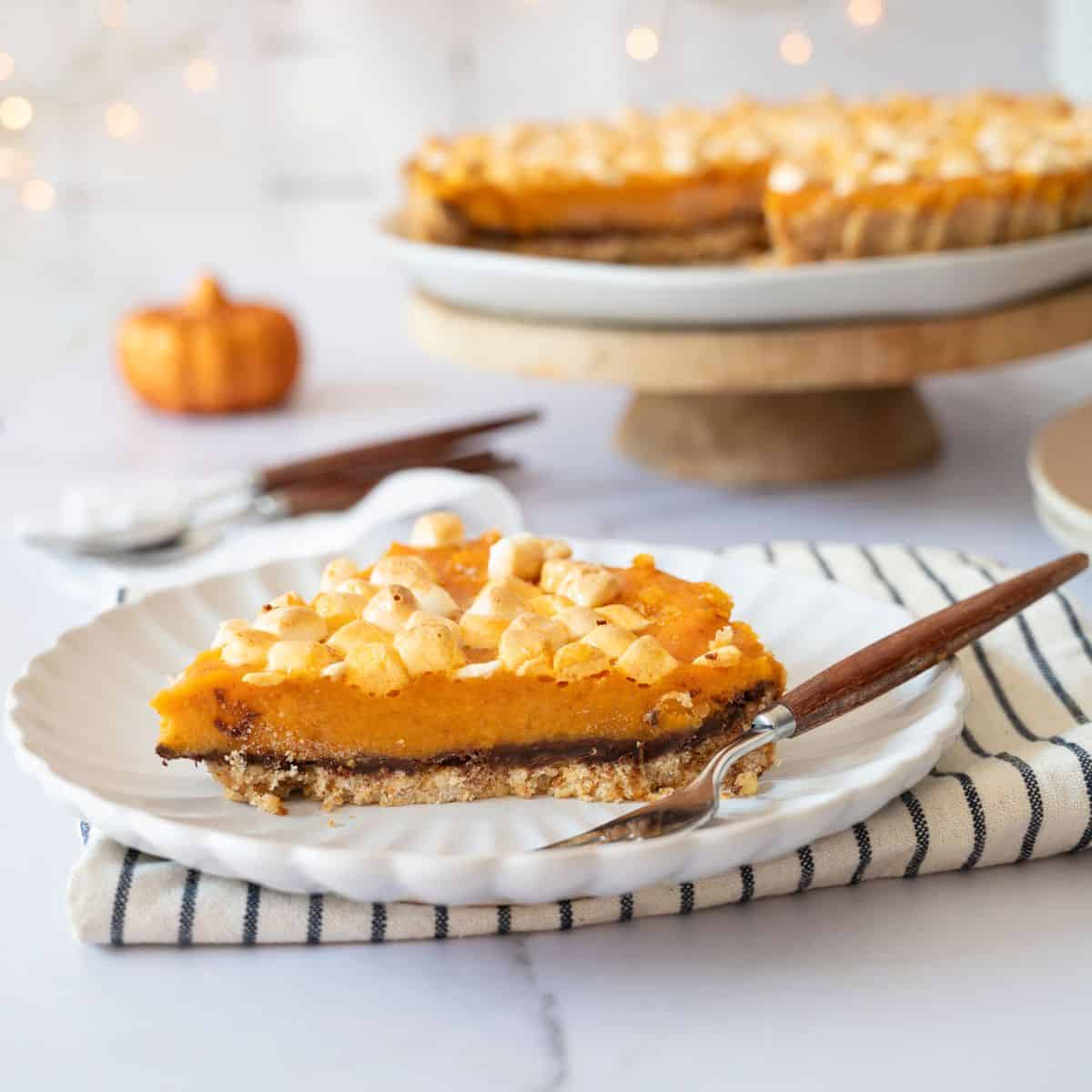 A slice of sweet potato pie served on a plate with the whole pie blurred in the background.
