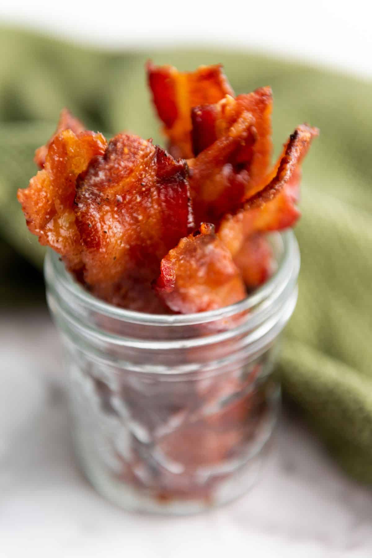 Candied bacon served in a jar with a cloth in the background.