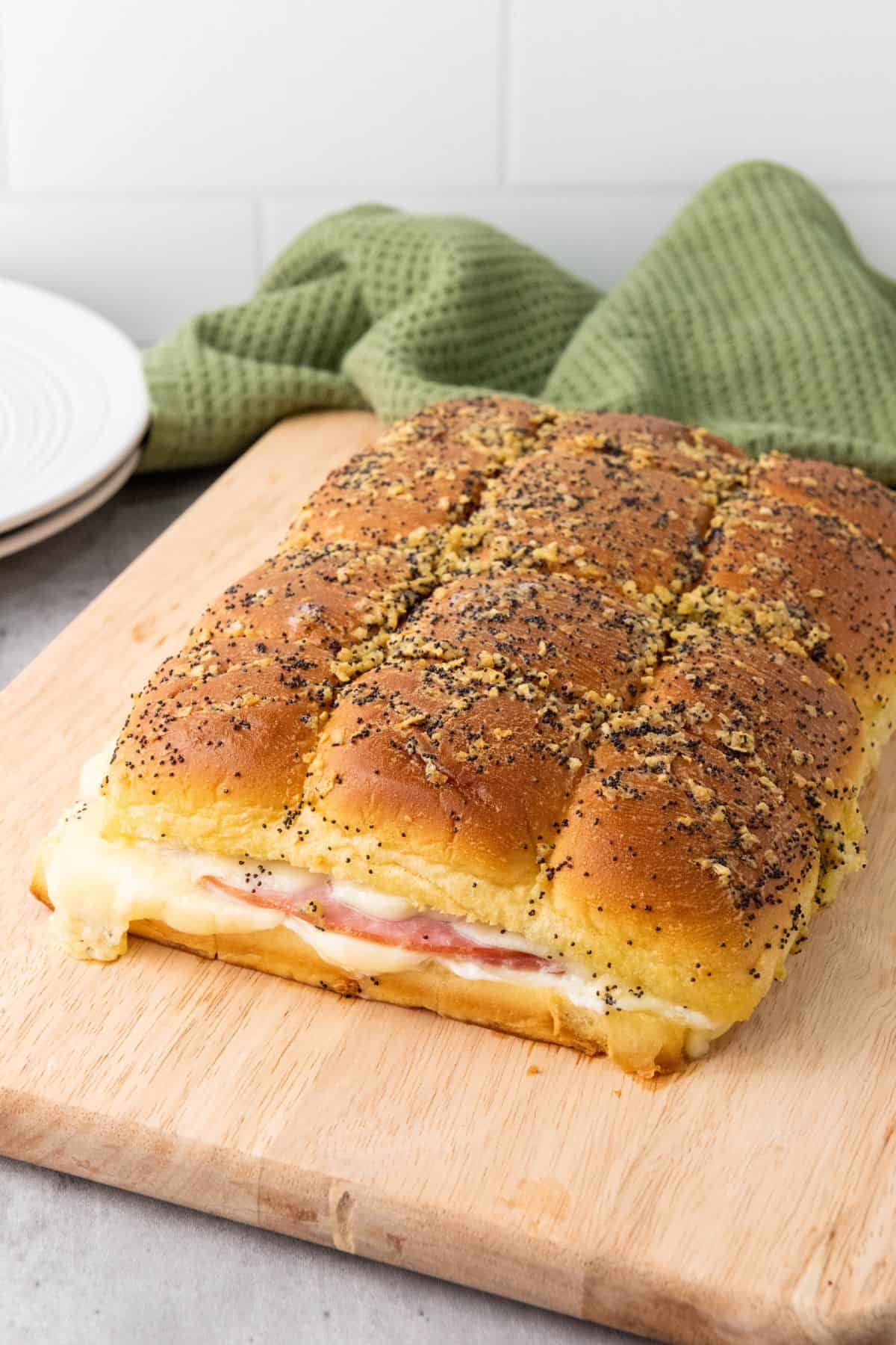 Warm melty ham and cheese sliders served on a wooden board, showing layers of gooey cheese and savory ham inside soft rolls.