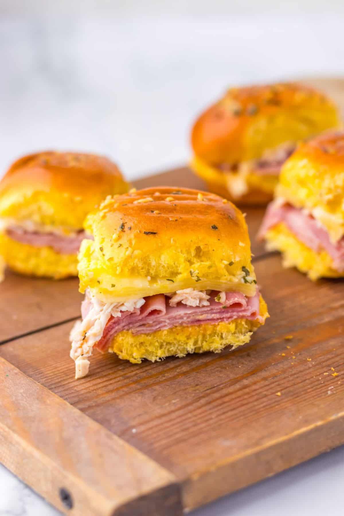 Chicken Cordon Bleu sliders on Hawaiian rolls arranged on a wooden board.