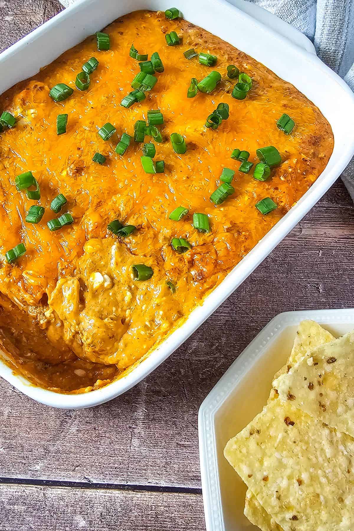 Hot chili cheese dip in a serving dish with tortilla chips on the side.
