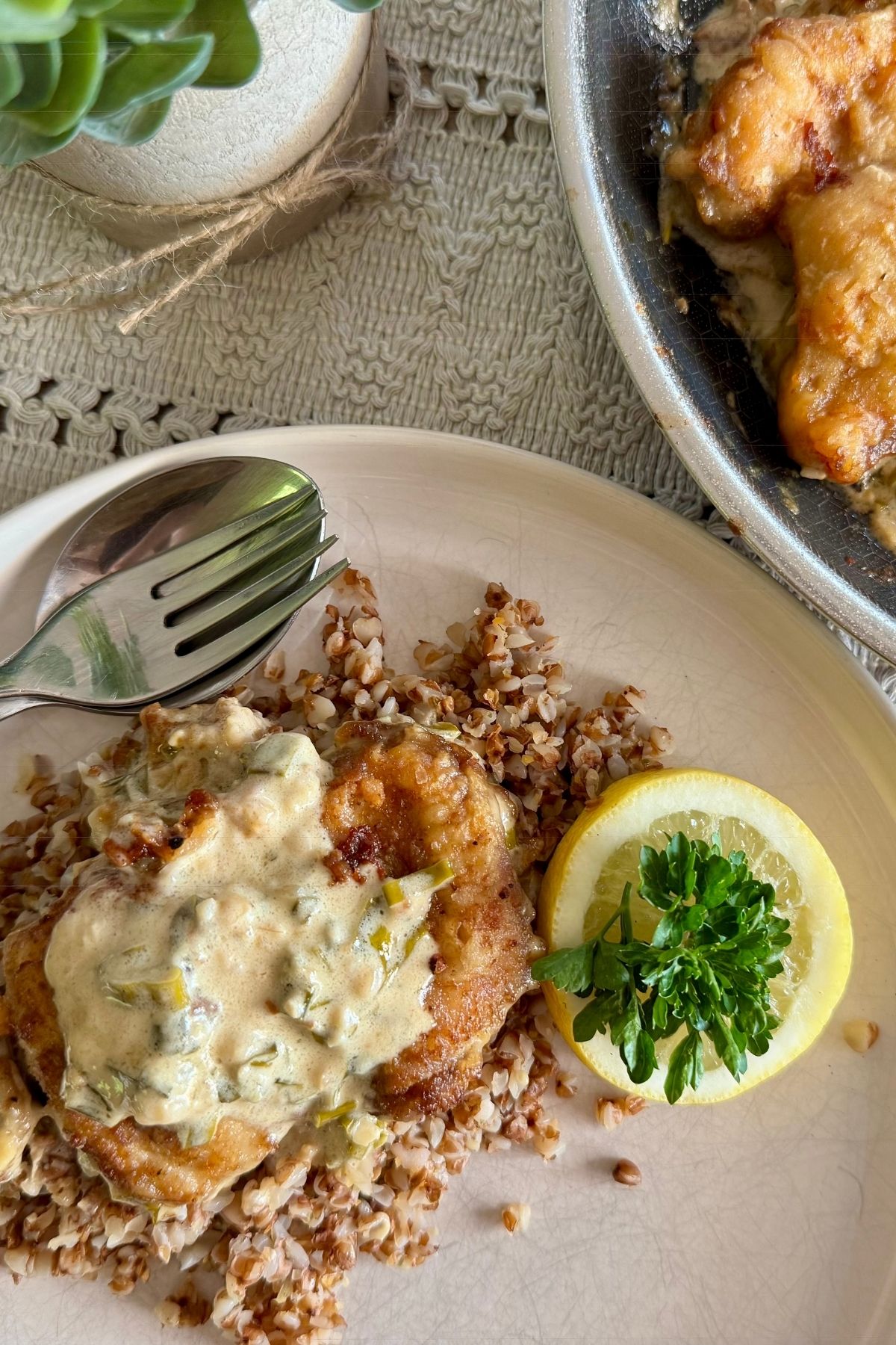 Creamy lemon chicken served with buckwheat on a plate, with extra portions in the pan beside it.