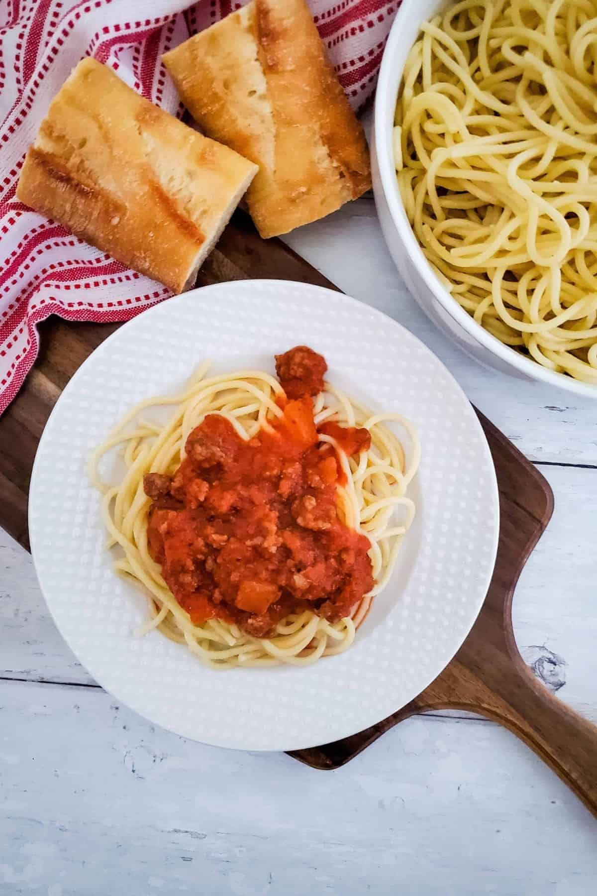 Beefy spaghetti served on a plate with bread on the side.