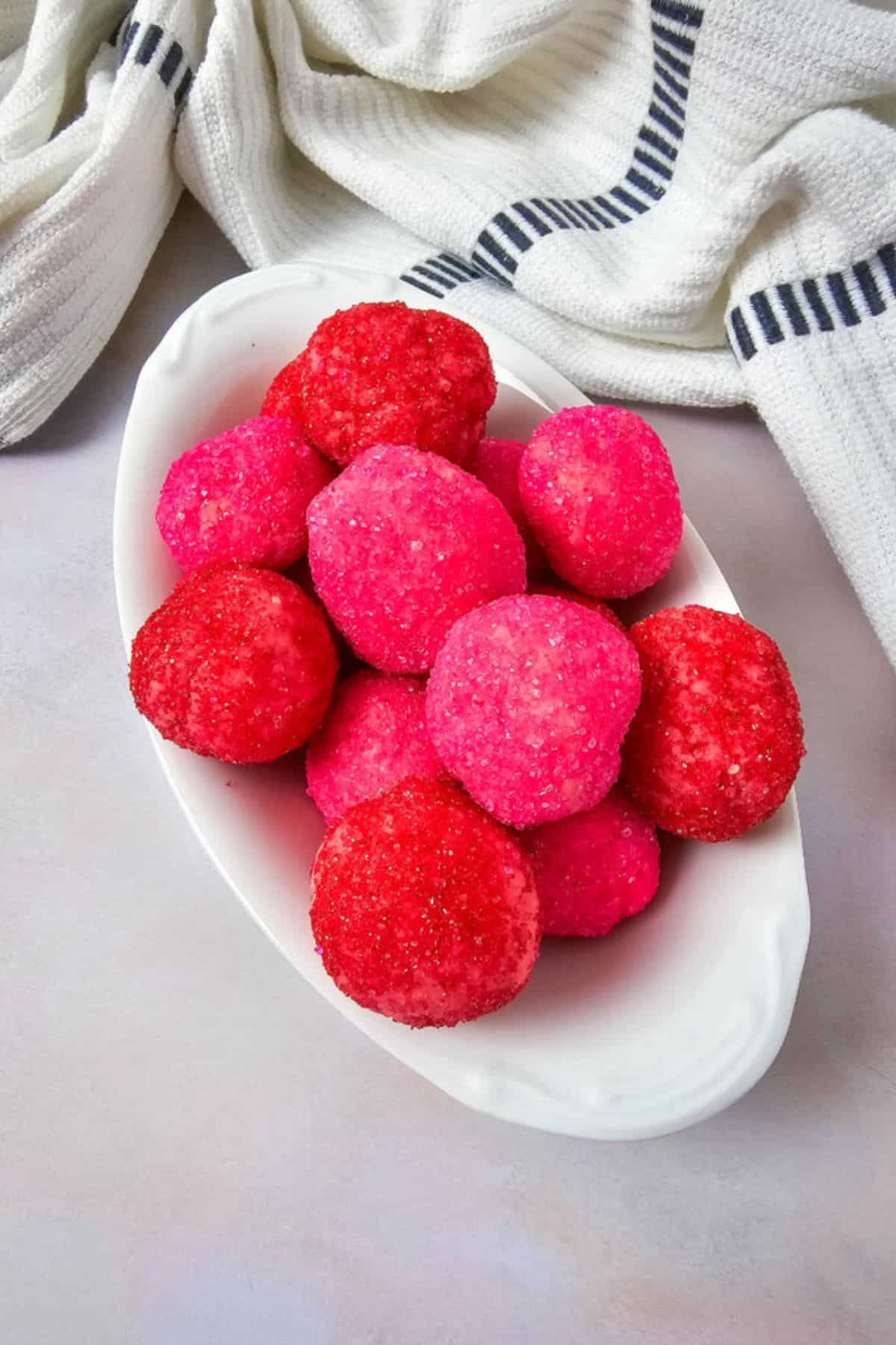Vibrant pink and red frosted cake pops arranged on a white dish, with a cozy striped cloth behind, perfect for dessert photos.
