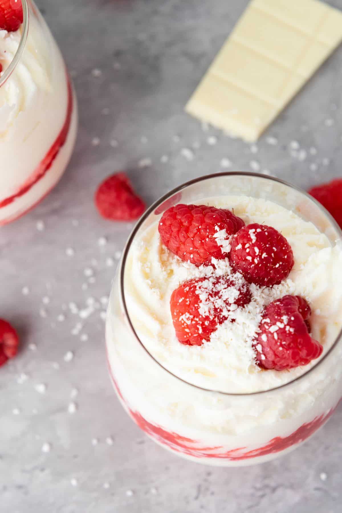 Close-up of a creamy strawberry parfait topped with fresh raspberries and white chocolate shavings.