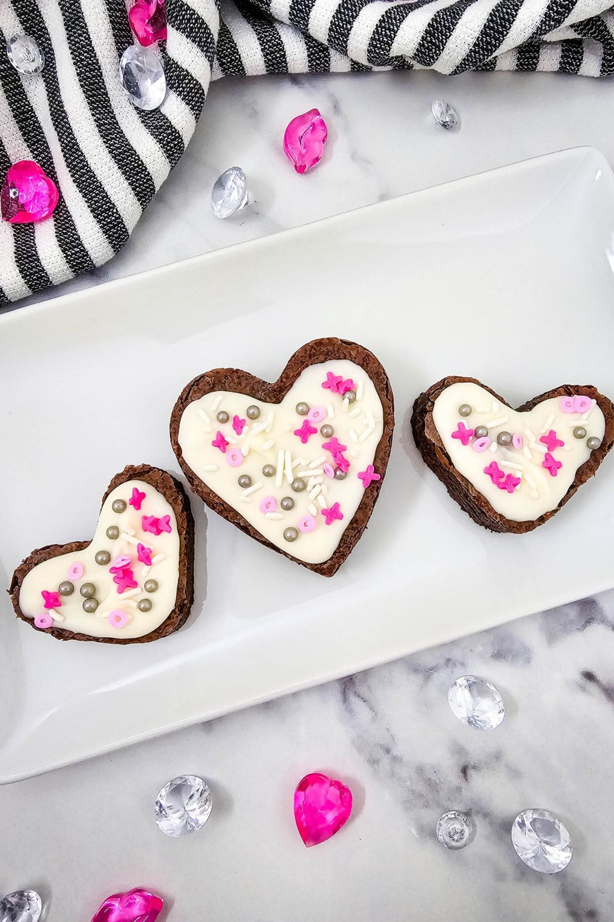 Delicious heart-shaped cookies decorated with white icing and pink, silver, and purple sprinkles.