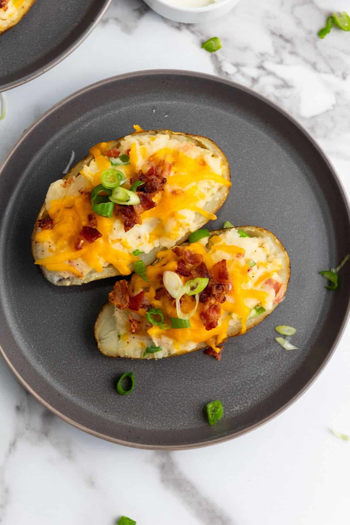 Delicious baked potato skins topped with melted cheese, bacon bits, and green onions in a black bowl.