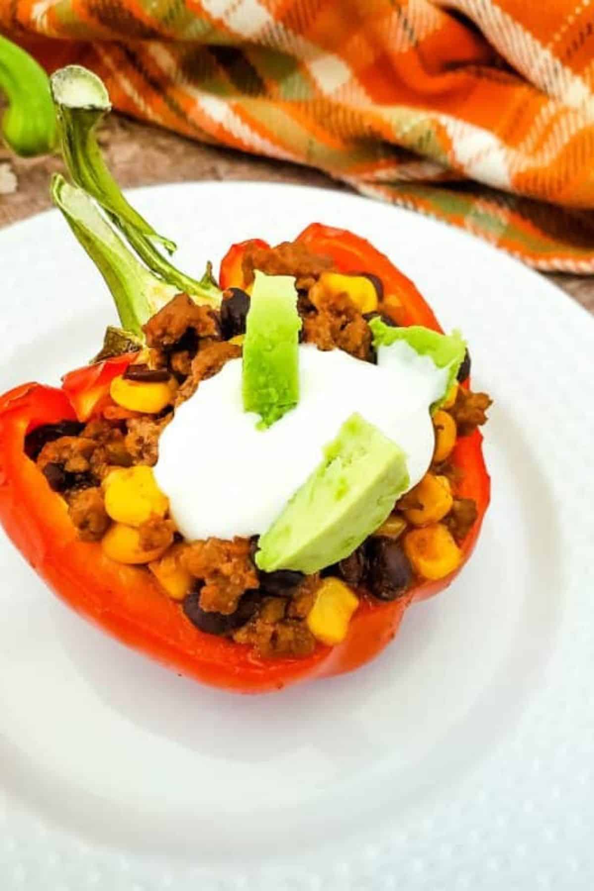 Bright stuffed bell pepper filled with cooked ground meat, corn, and black beans topped with sour cream, avocado, and green onion.