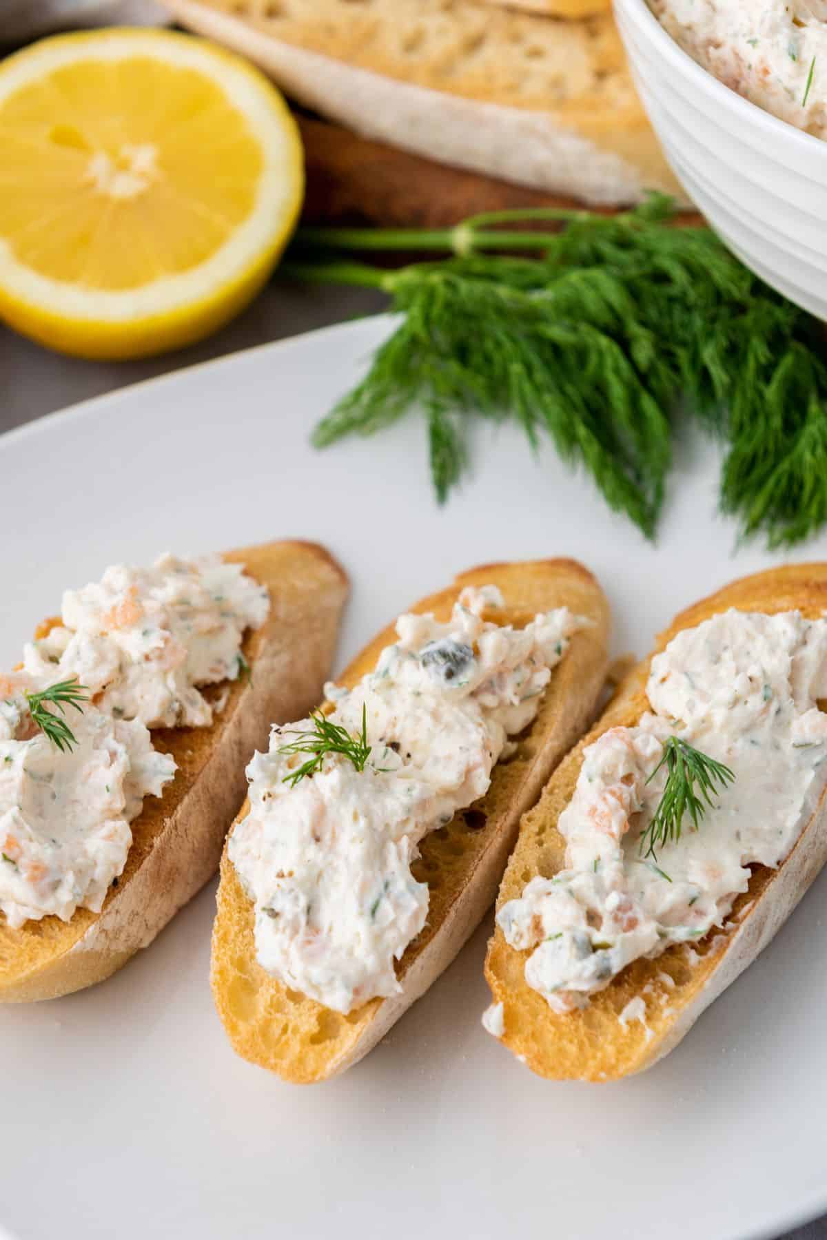 Creamy lobster salad on toasted baguette slices garnished with herbs, served with lemon and fresh greens.