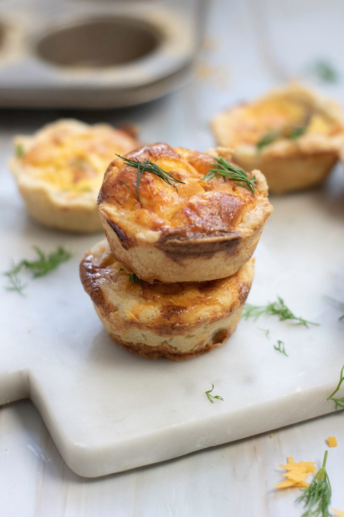 Delicious cheesy mini quiches garnished with herbs, served on a white cutting board.