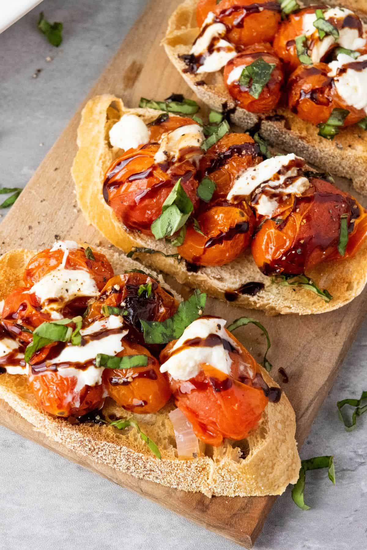 Close-up of toasted bread topped with cherry tomatoes, fresh basil, mozzarella, and balsamic glaze.