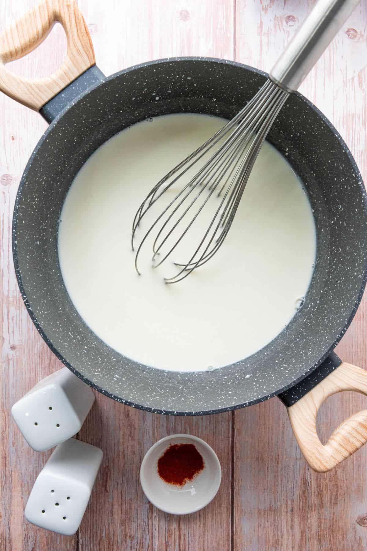 Mixture cooking in a saucepan with a whisk resting on the edge.