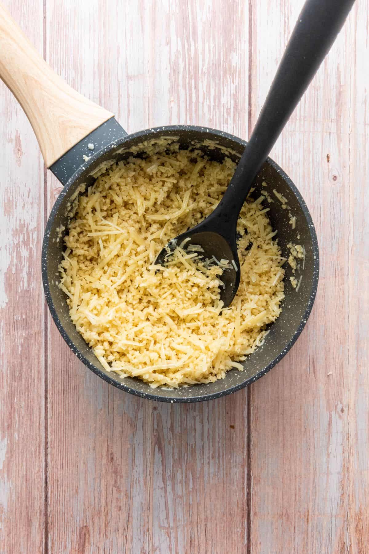 Cheese melting in a pot on a wooden table with a black spatula.