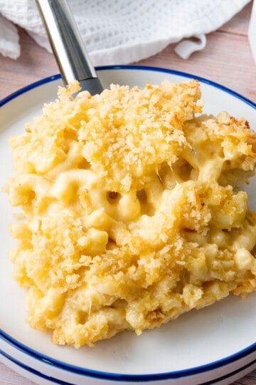 A spatula lifting a portion of creamy baked macaroni and cheese over a white plate.