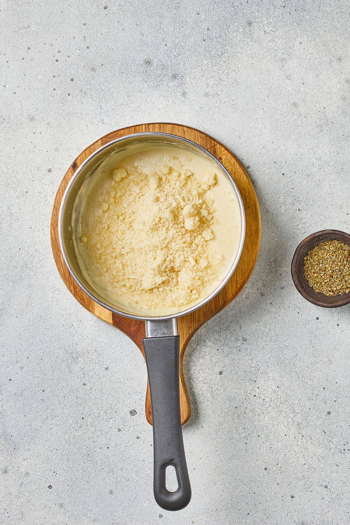 A close-up of melted cheese in a pot on a cutting board with seasonings for cooking or baking.