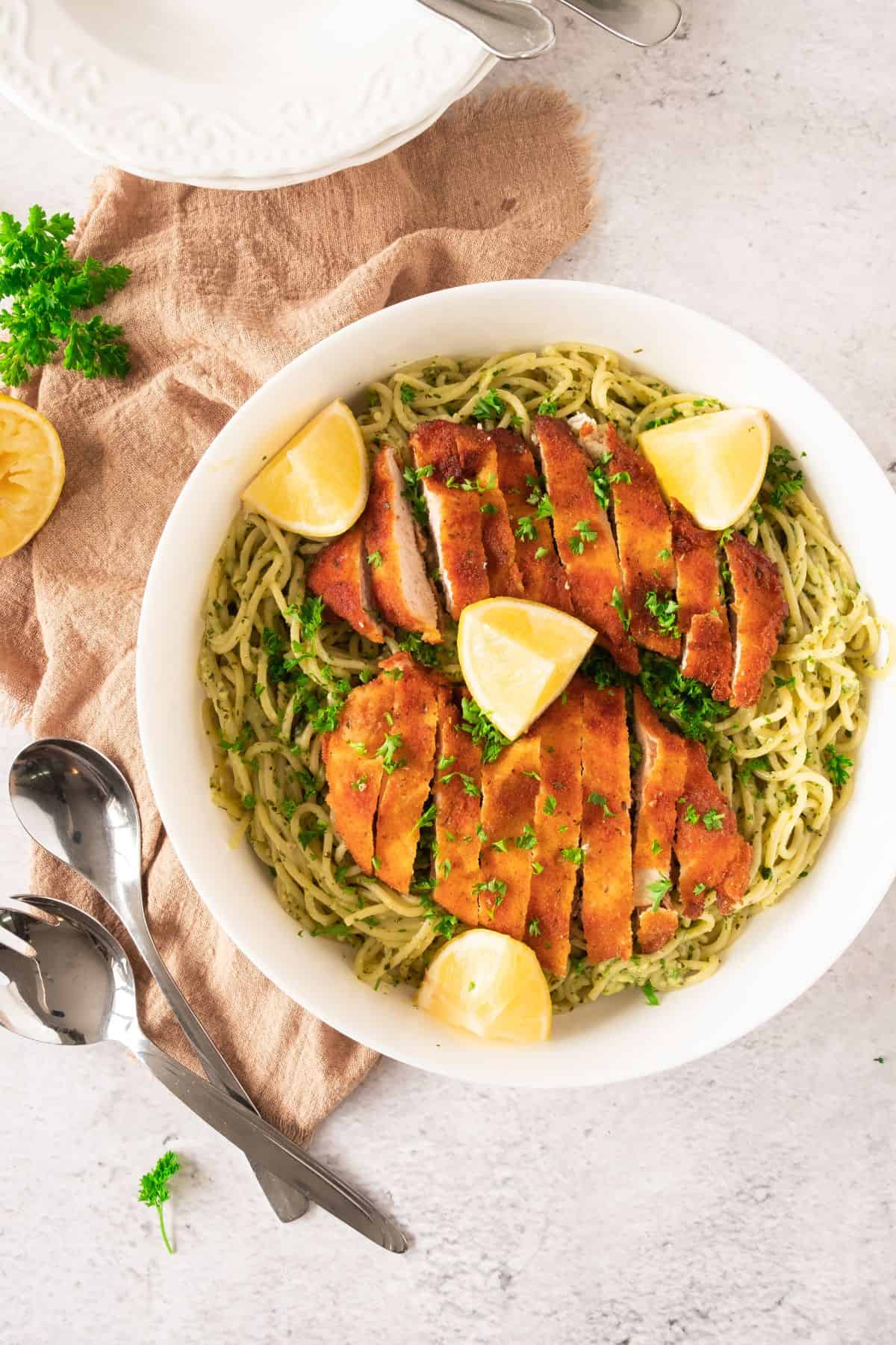 Delicious spaghetti dish featuring crispy chicken, lemon, and herbs on a white plate.
