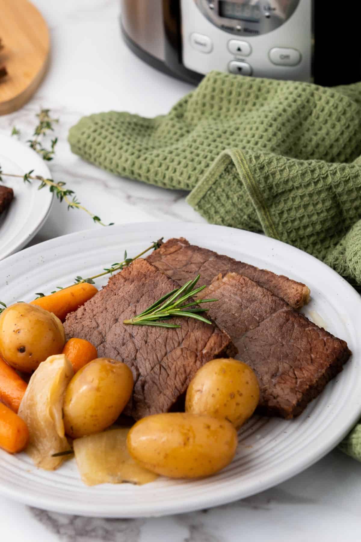 A delicious beef roast served with potatoes and carrots on a white dish, with green herbs for garnish, placed on a marble surface.