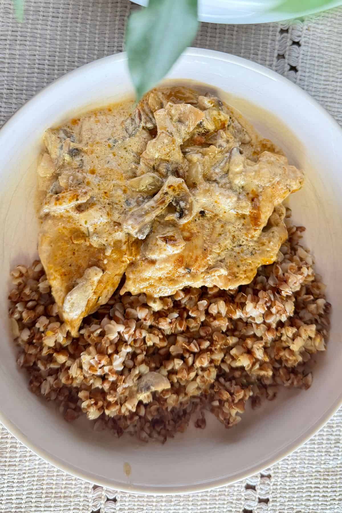 Close-up of chicken with mushroom cream sauce served over buckwheat in a white bowl.