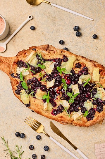 Delicious homemade berry fruit flatbread with cheese and fresh herbs on a rustic platter. Perfect for a sweet, savory snack or meal.