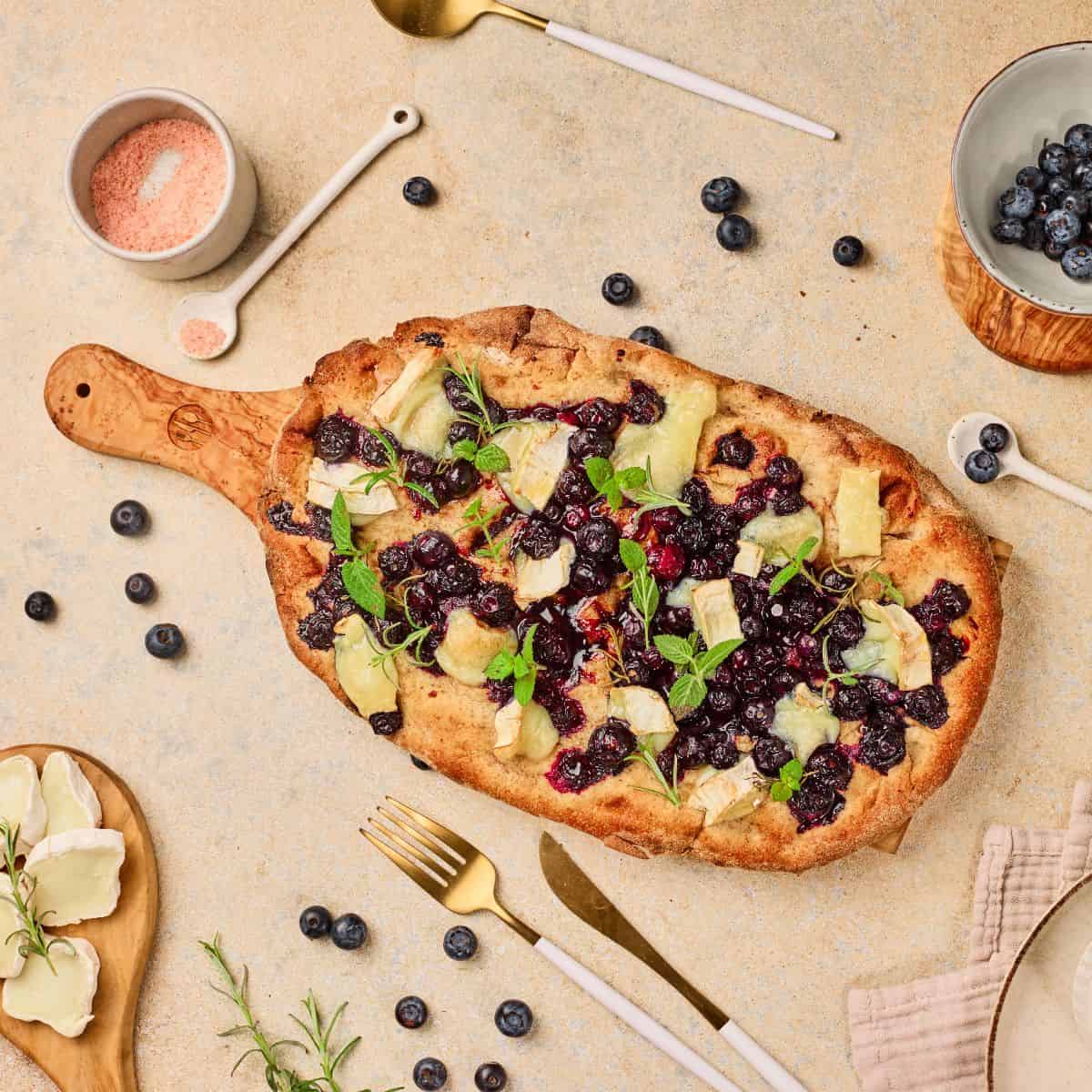 Delicious homemade berry fruit flatbread with cheese and fresh herbs on a rustic platter. Perfect for a sweet, savory snack or meal.
