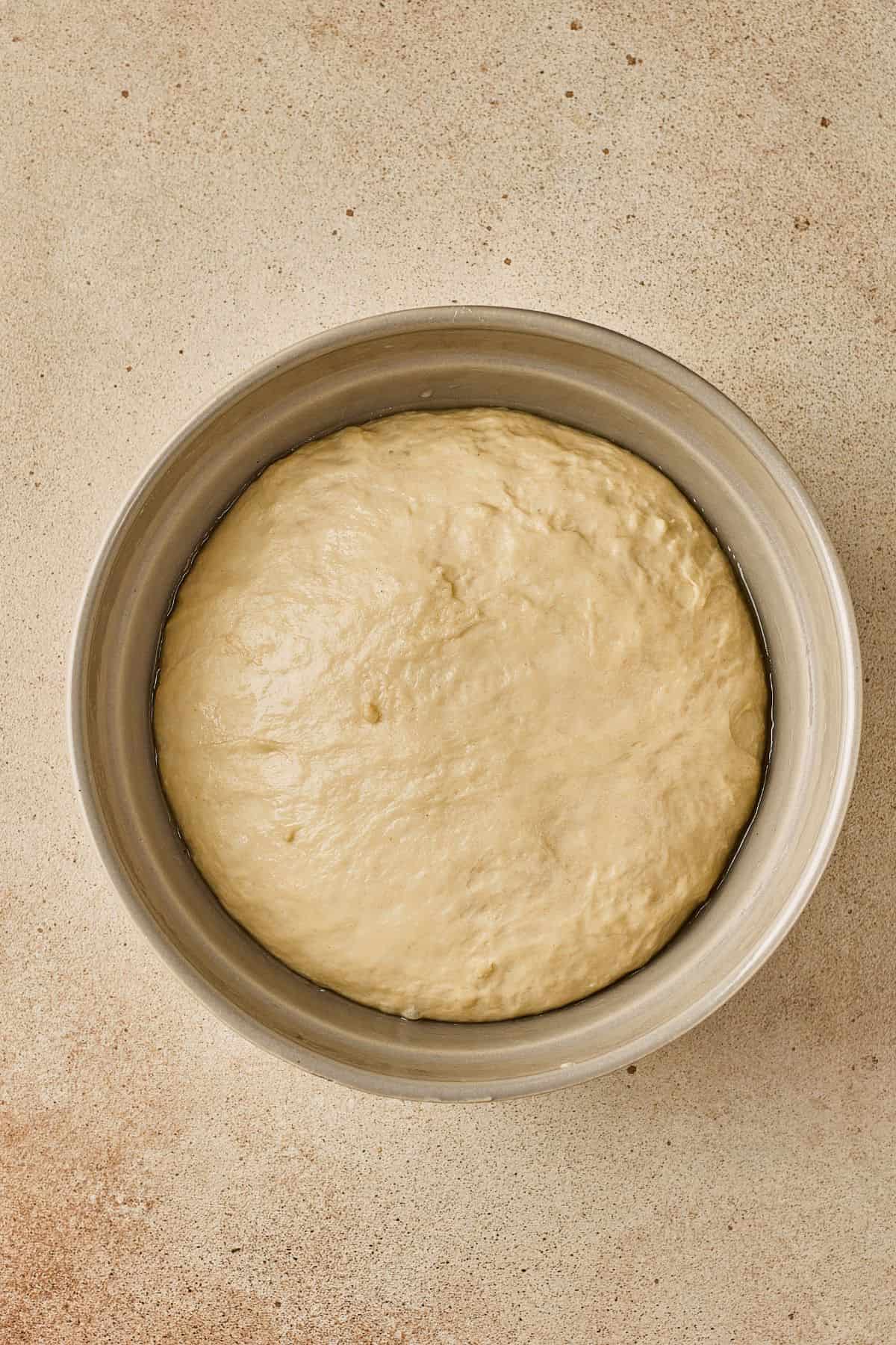 Bowl of rising bread dough on a beige countertop for baking at home.