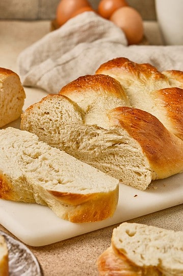 Freshly baked bread loaf with slices on a marble board, set in a cozy kitchen with eggs and rustic decor behind.