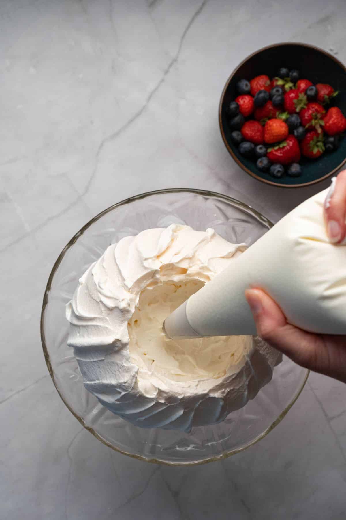 Hand piping whipped cream into a bowl for dessert topping.