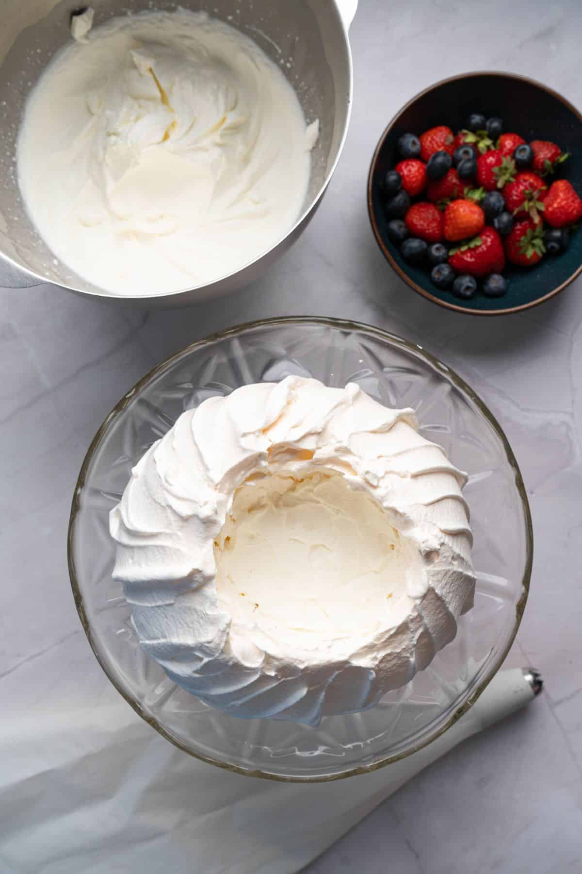 Cream cheese frosting in a glass bowl with berries in a black bowl upstairs.