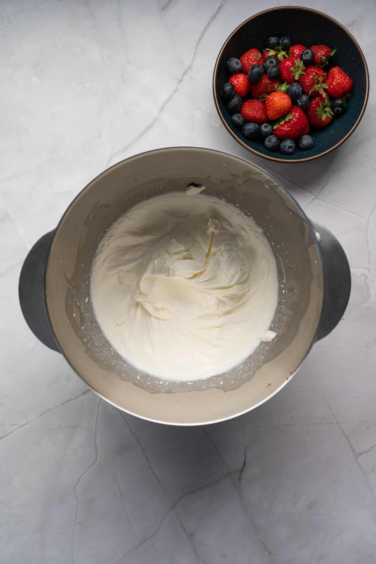 Delicious whipped cream with strawberries and blueberries in a bowl, perfect for desserts or topping.