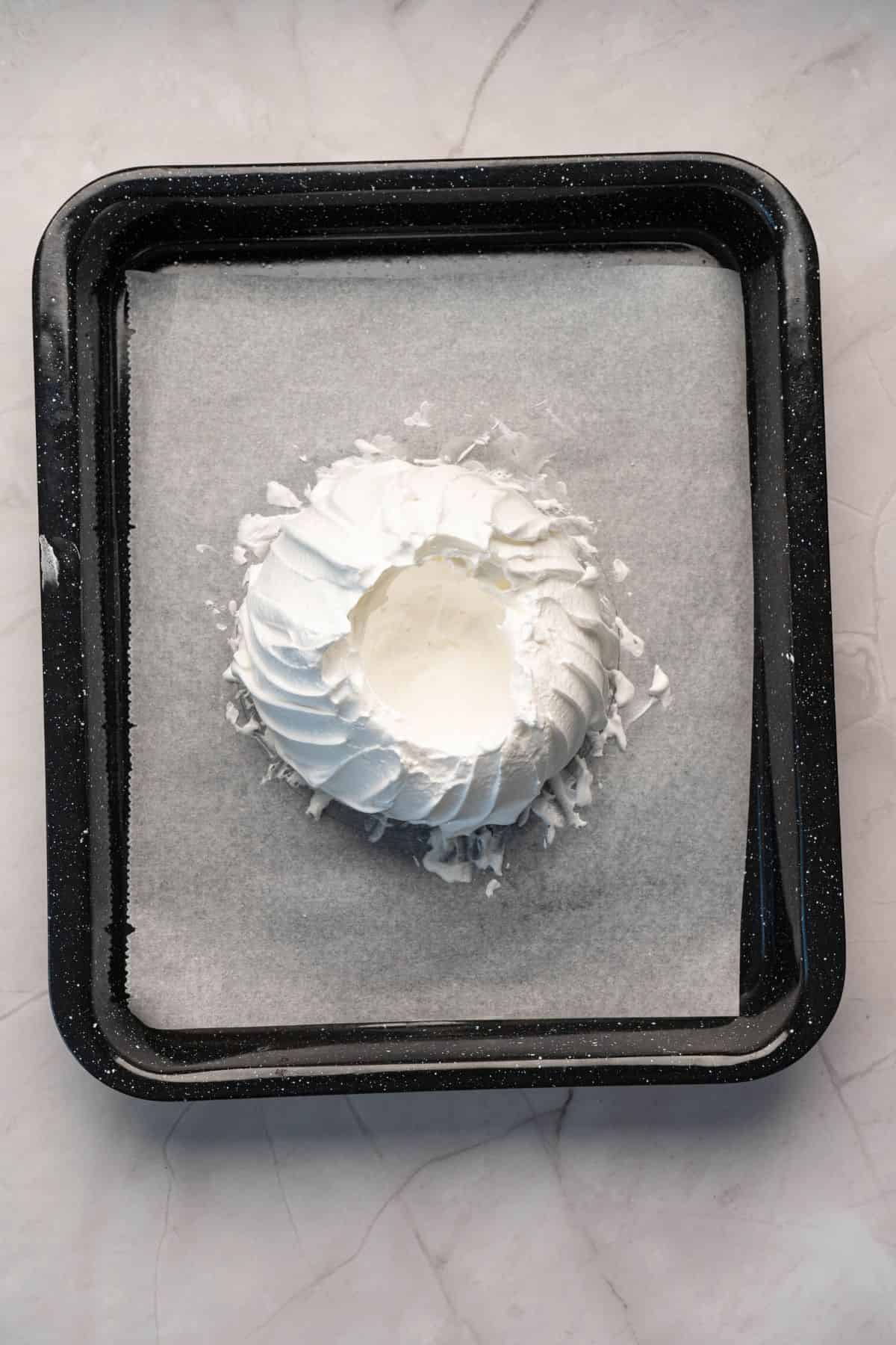 Close-up of fluffy whipped cream in a bowl on a baking tray.