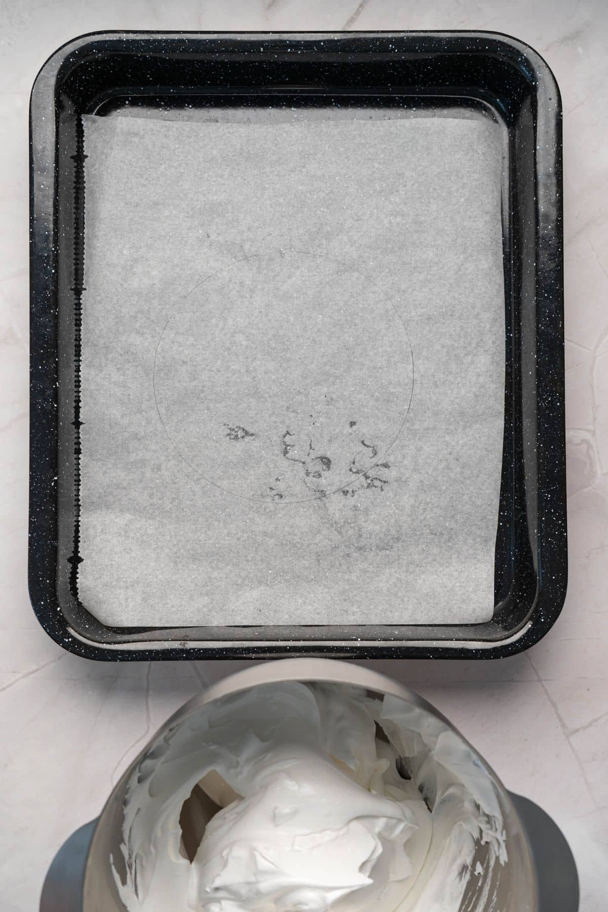 Lightly greased baking pan prepared with parchment for dessert, with fresh whipped cream in the mixer.