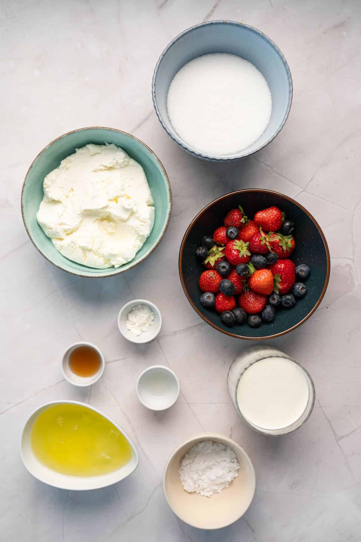 Bright and colorful fresh berries, cream cheese, sugar, and other ingredients laid out for homemade dessert.