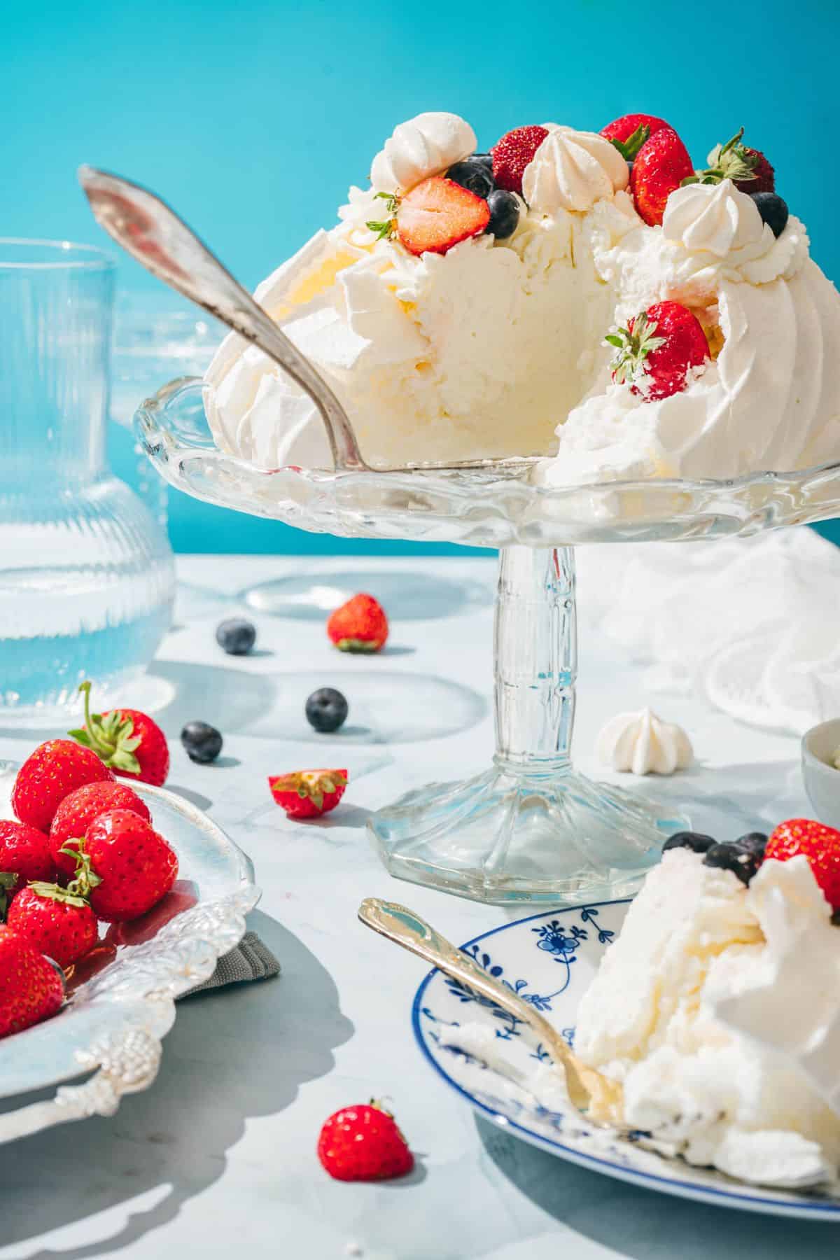 Delicious berry cheesecake topped with strawberries, blueberries, and whipped cream on a glass cake stand.