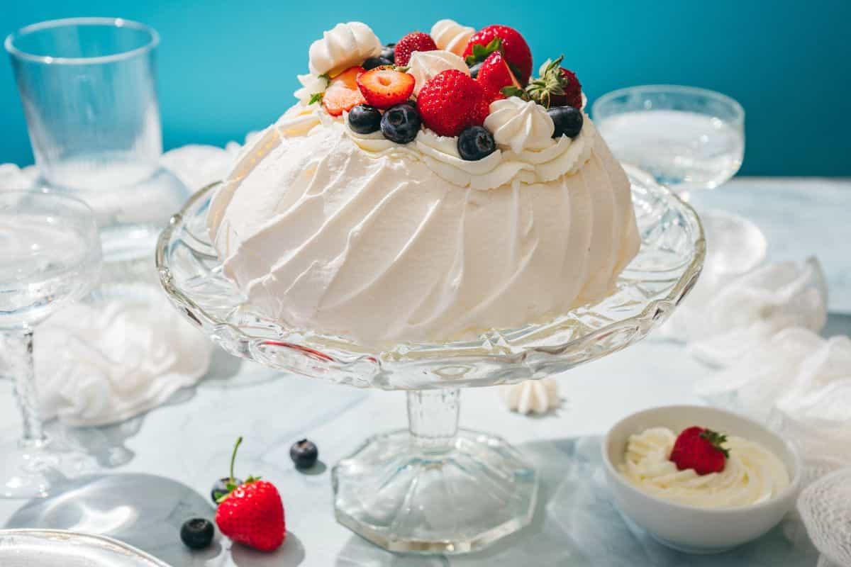 Delicious meringue with fresh strawberries, blueberries, and whipped cream on a glass platter.