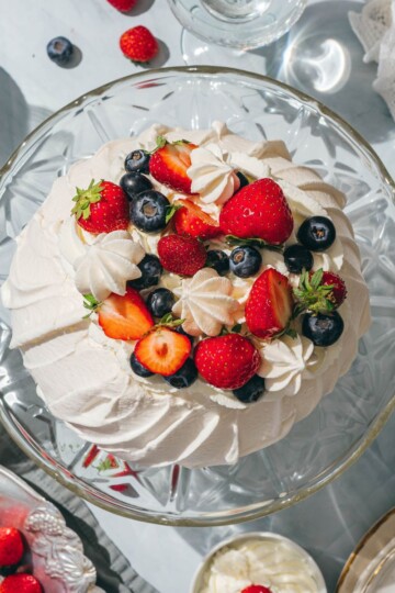 Top view of pavlova topped with whipped cream and fresh berries.