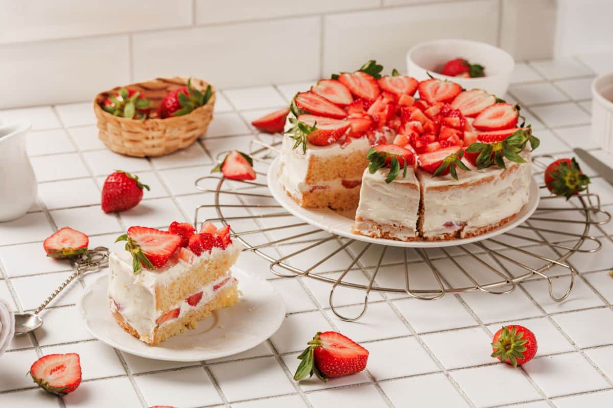 Delicious strawberry cake with fresh fruit topping displayed on a white plate with a slice cut out.