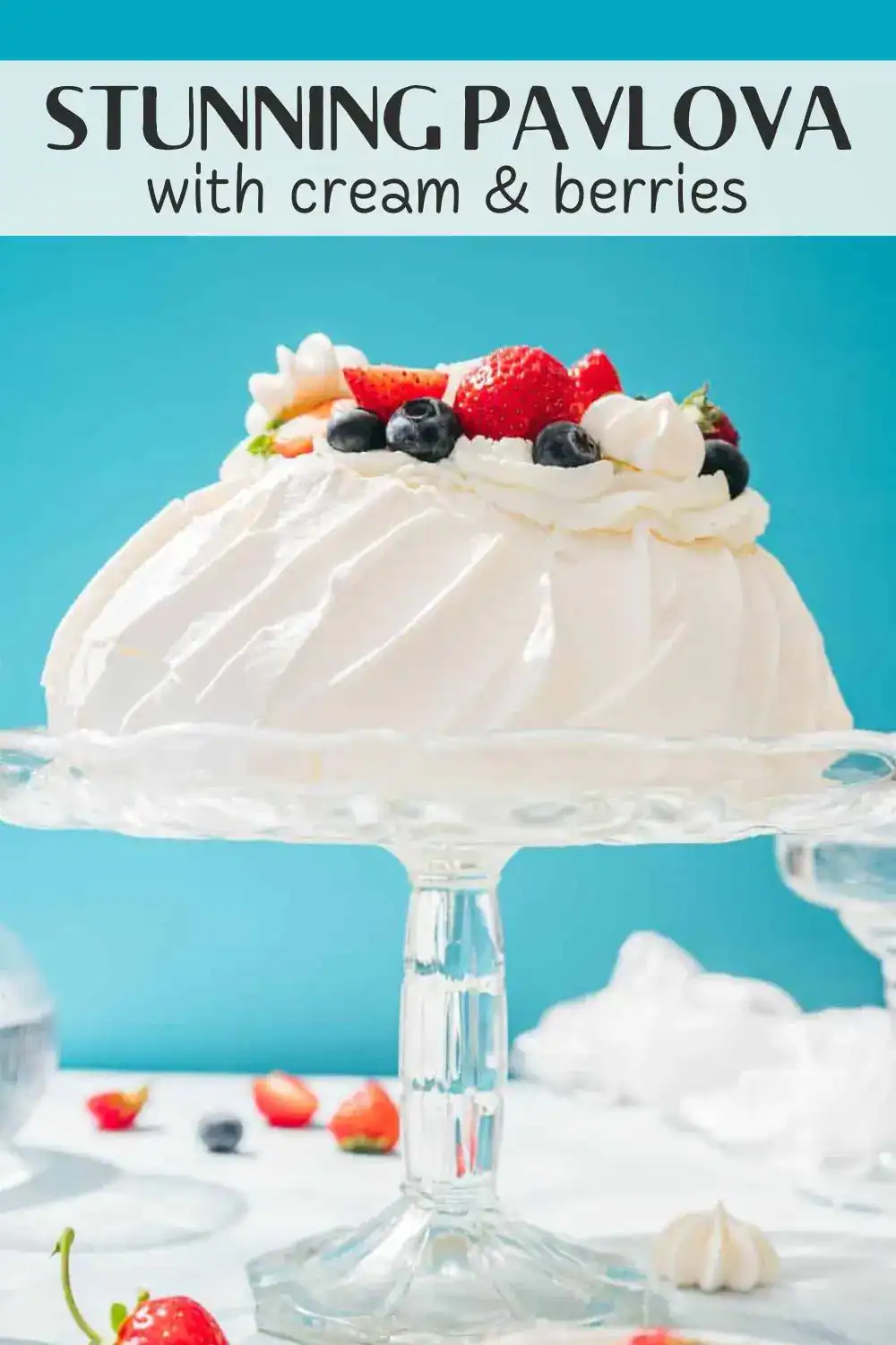 Bright Pavlova with fresh strawberries, blueberries, and whipped cream on a glass cake stand.