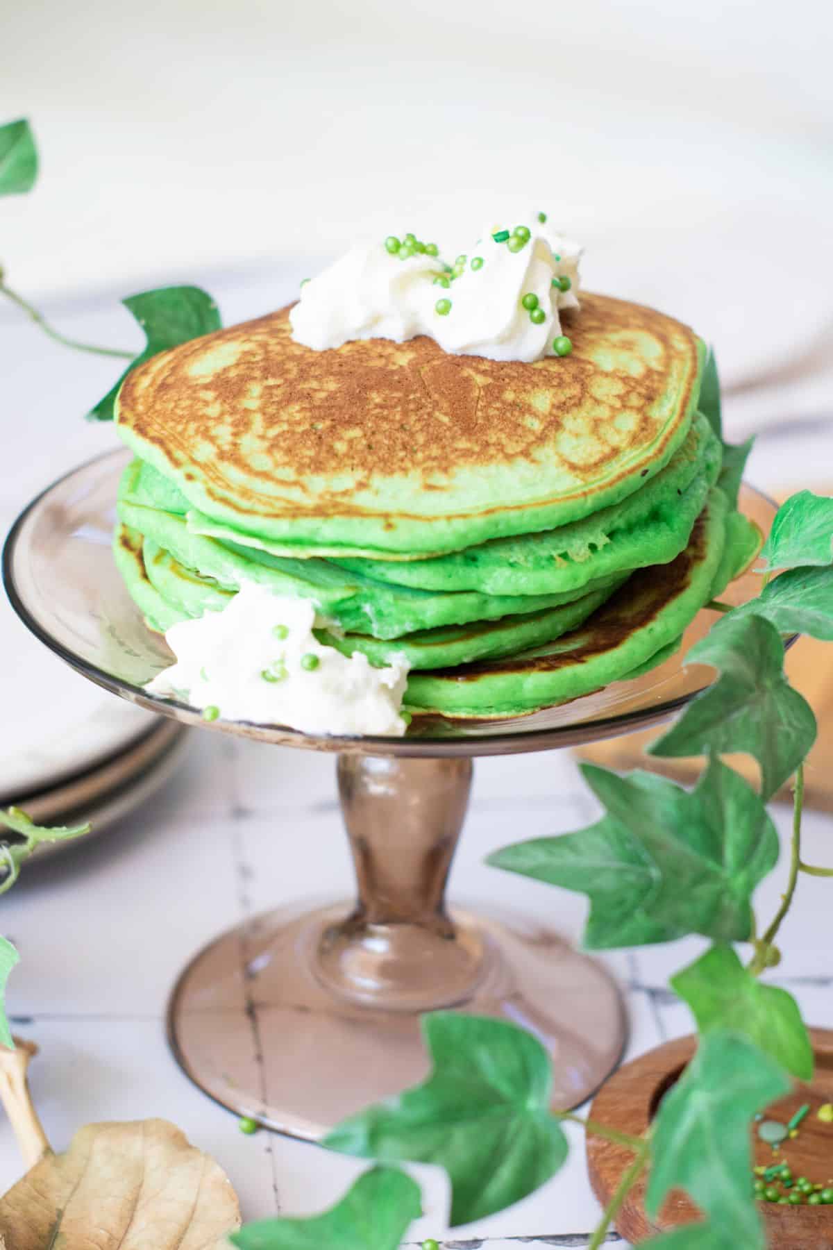 Bright green pancakes for St. Patrick's Day celebration, served on a glass cake stand.
