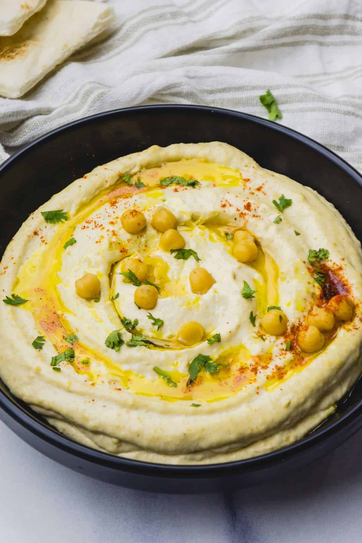Creamy hummus topped with chickpeas, olive oil, and herbs in a black bowl.