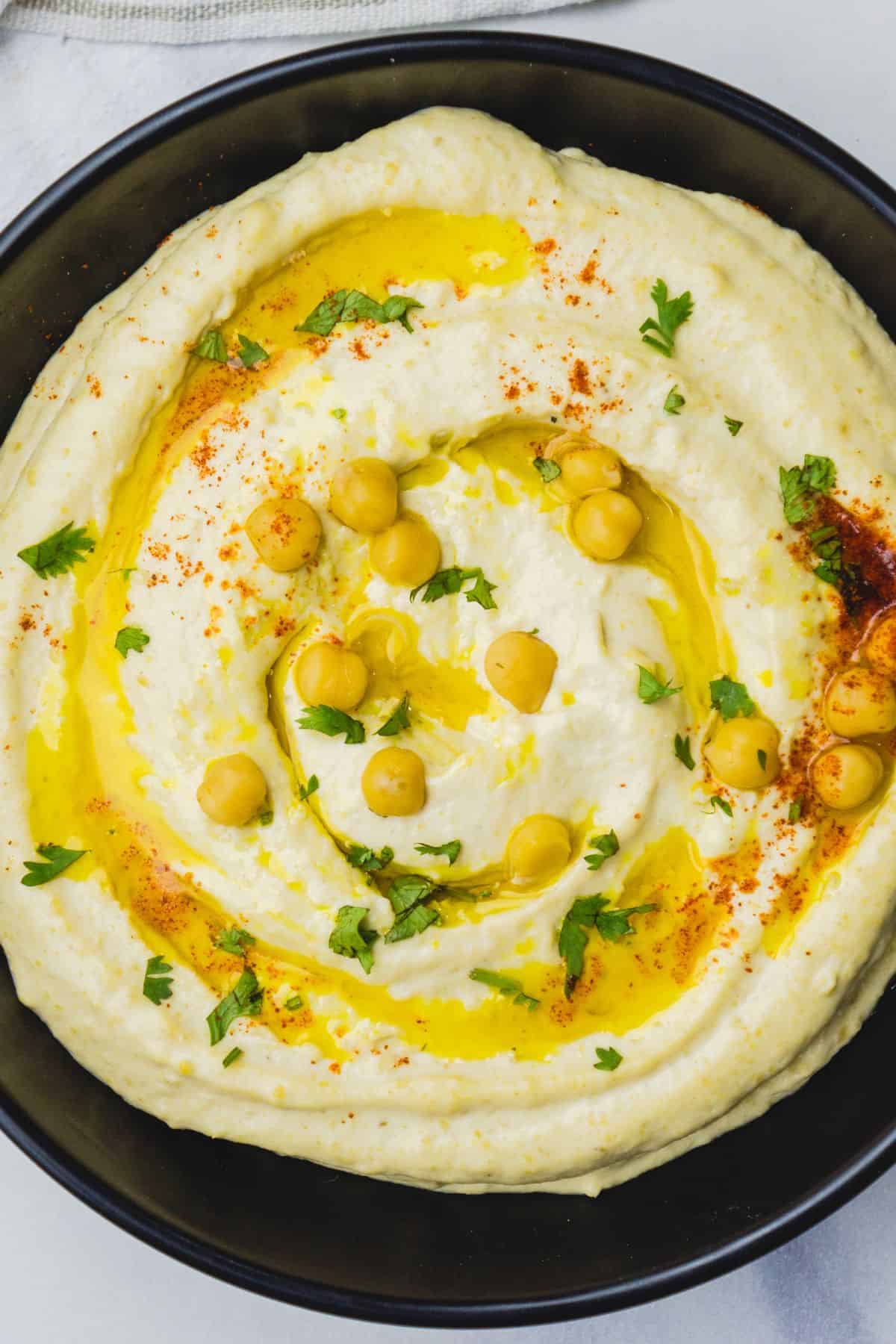Smooth hummus topped with olive oil, chickpeas, parsley, and paprika for a flavorful appetizer.