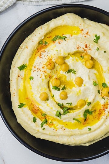 Vegan hummus topped with olive oil, chickpeas, and herbs in a black bowl.