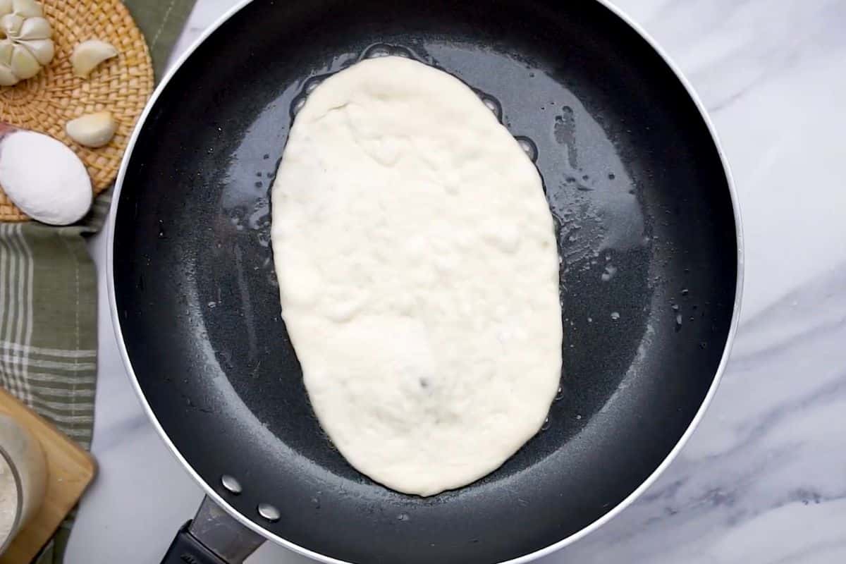 Homemade pizza dough cooks in a frying pan on a stovetop for quick delicious pizza.