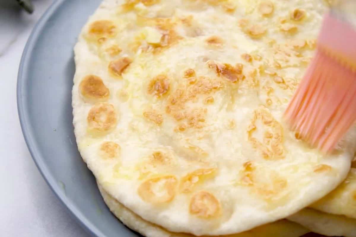 A baking spoon brushes melted cheese onto freshly baked cheese bread in a baking dish.