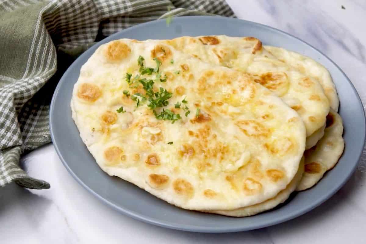 Delicious homemade cheese naan bread garnished with fresh herbs on a stylish blue plate.